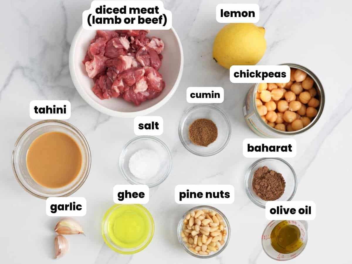 ingredients needed to make hummus with meat, including canned chickpeas, diced meat, lemon, garlic, olive oil, tahini, pine nuts, ghee, salt, cumin, and baharat.