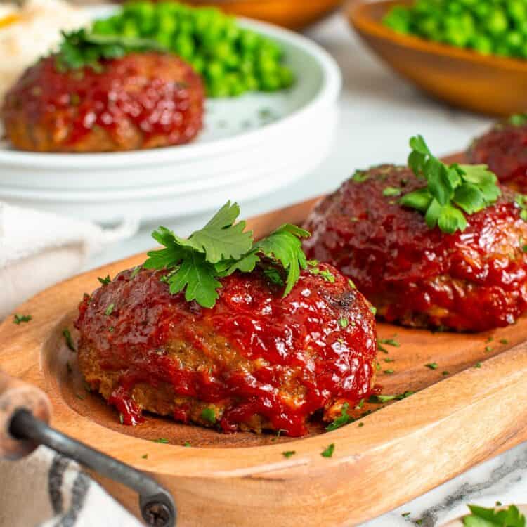 round mini meatloaves with ketchup glaze on an oval shaped wooden board.