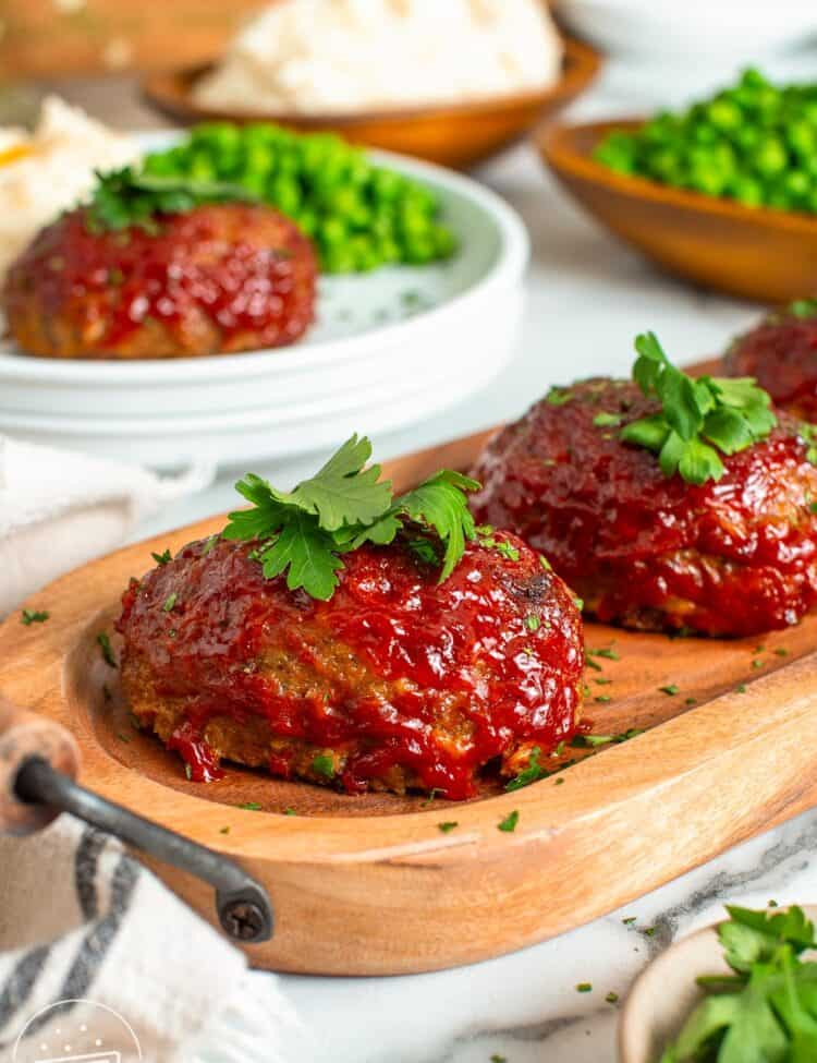 round mini meatloaves with ketchup glaze on an oval shaped wooden board.
