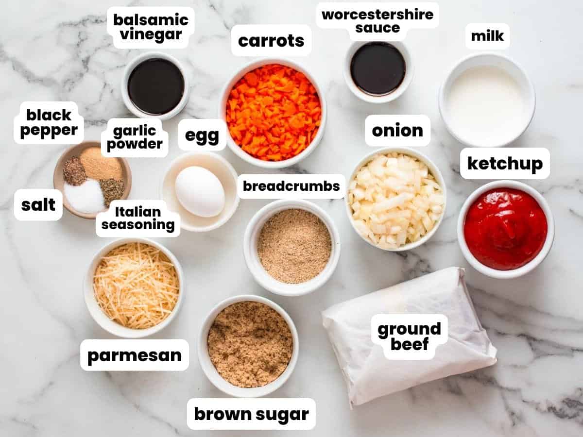 The ingredients for mini meatloaf, including ground beef, ketchup, breadcrumbs, and seasonings. All are measured into small bowls, arranged on a marble counter, and labeled.