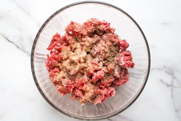 ground beef in a glass bowl with seasonings and breadcrumbs.
