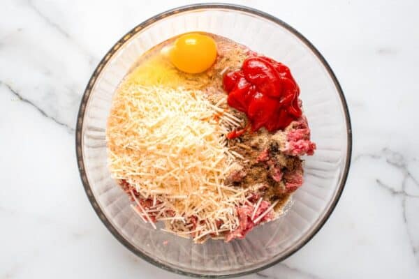 parmesan, egg, and ketchup added to meatloaf mixture in a glass bowl.