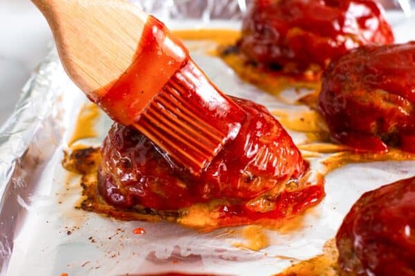 a pastry brush adding extra glaze to mini meatloafs after they've been baked.