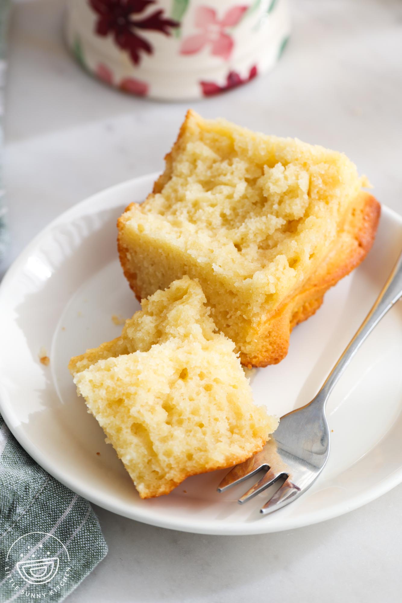 a slice of yogurt pound cake on a small white plate with a silver fork. The piece has been torn to show the dense, moist crumb structure.