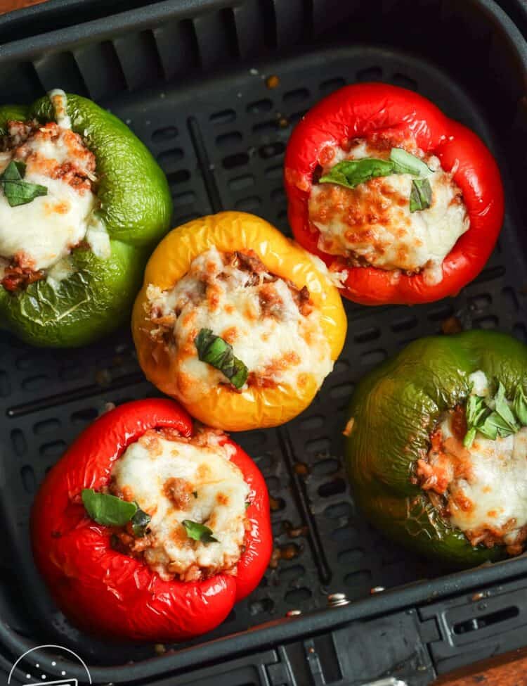 5 stuffed peppers (2 red, two green, and one yellow) in the basket of a square air fryer.