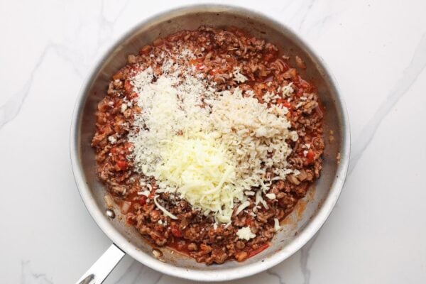 rice and cheese added to meat sauce in a skillet.