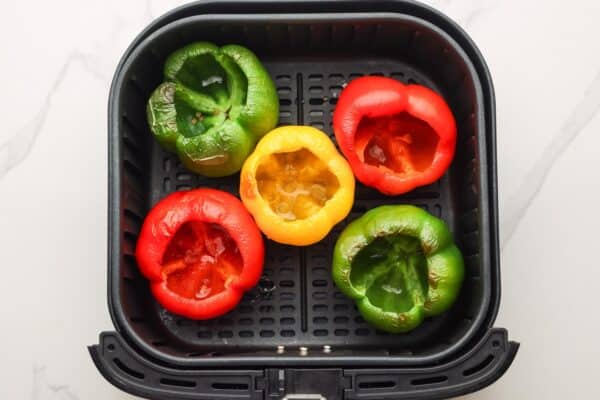 partially cooked bell peppers ready for stuffing, in a square black air fryer basket.