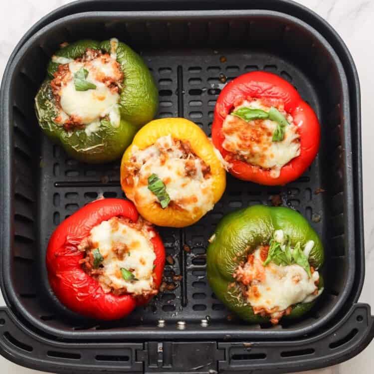 5 stuffed peppers in an air fryer, topped with melted, browned cheese.
