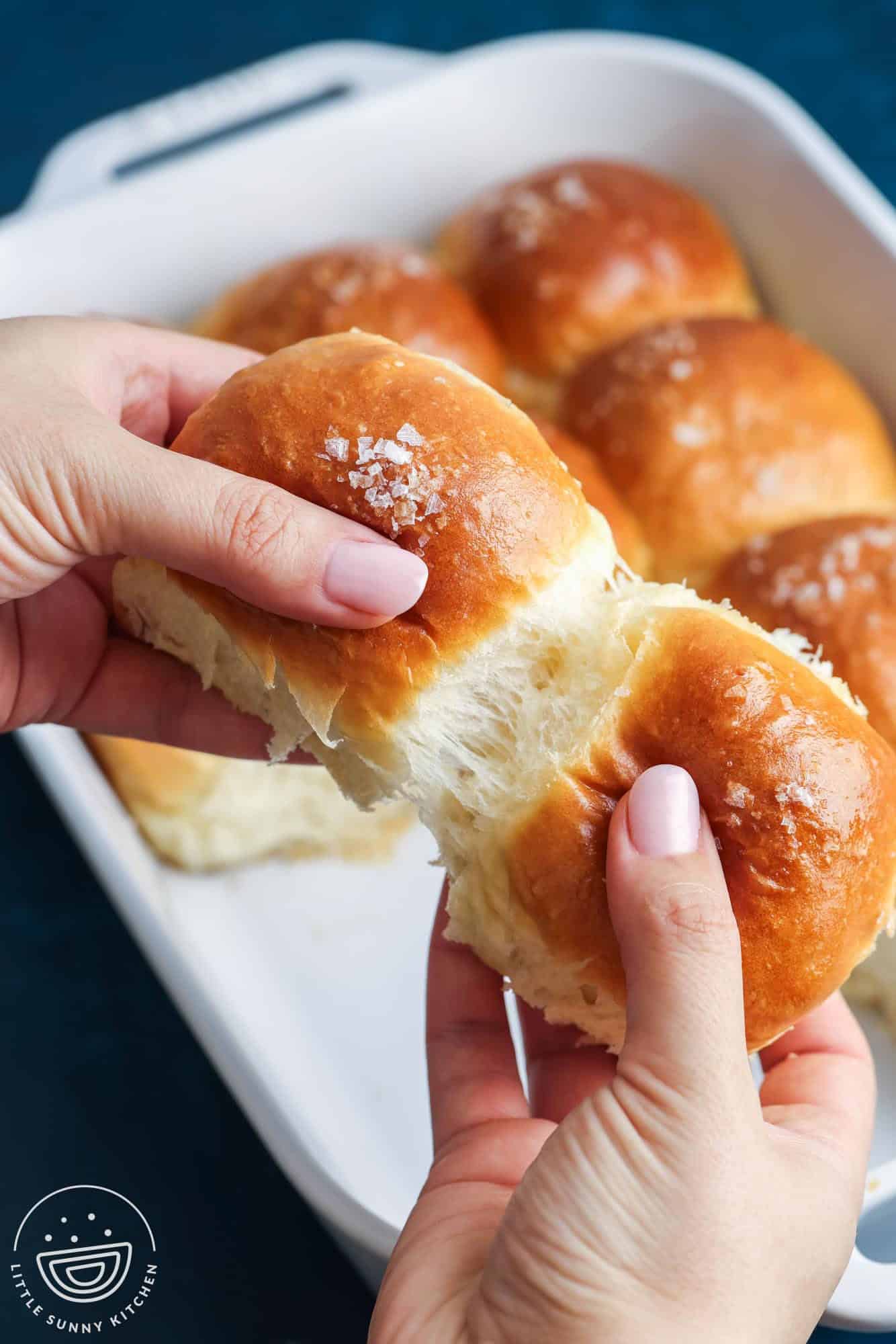 hands pulling apart two dinner rolls to show the airy, fluffy texture.