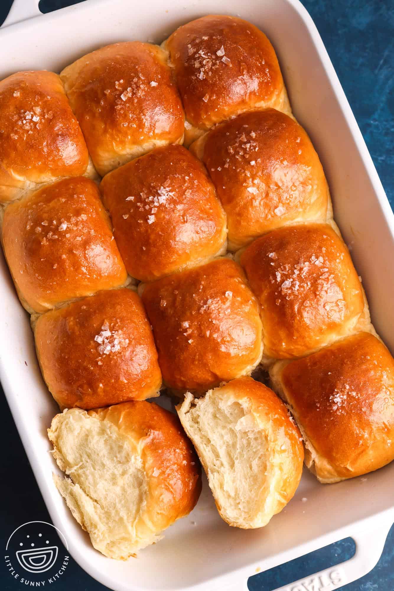 a pan of homemade dinner rolls. Two rolls have been pulled out and turned to the side to show the texture of the bread.