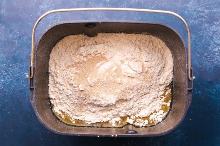 Ingredients for dinner roll dough in the pan of a bread machine. Yeast and flour are on top of the wet ingredients.