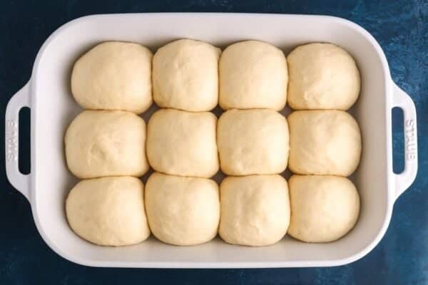Dinner rolls after second rise in a white ceramic baking dish. The dough is puffed up and fills the whole dish.