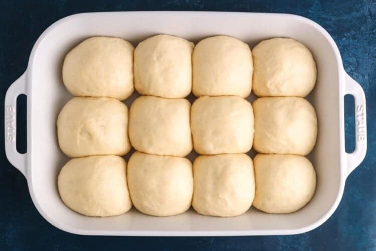 Dinner rolls after second rise in a white ceramic baking dish. The dough is puffed up and fills the whole dish.