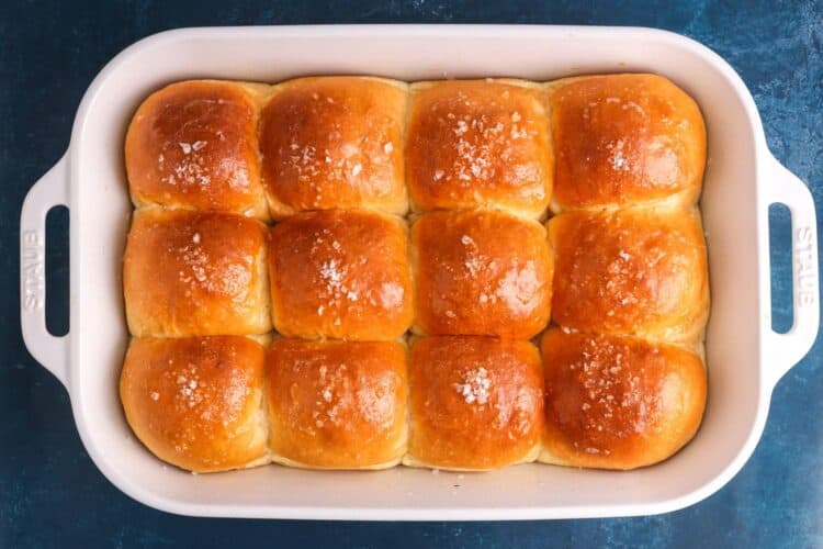 baked bread machine dinner rolls in a white ceramic baking dish. They are browned on top and sprinkled with coarse salt.