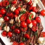 a sliced flank steak topped with a tomato and mozzarella caprese salad.