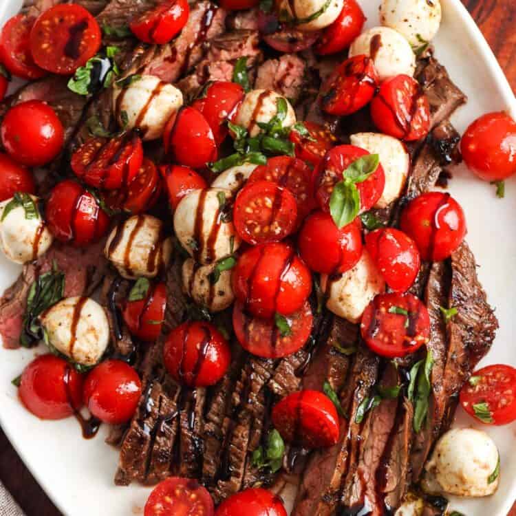 a sliced flank steak topped with a tomato and mozzarella caprese salad.