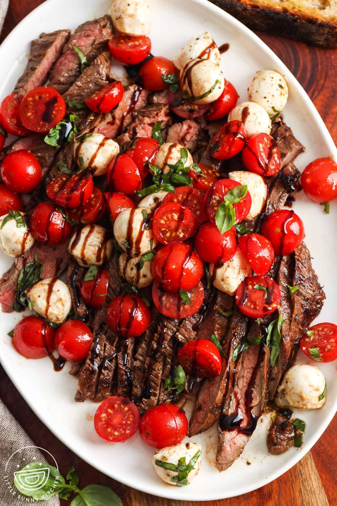 a sliced flank steak topped with a tomato and mozzarella caprese salad.