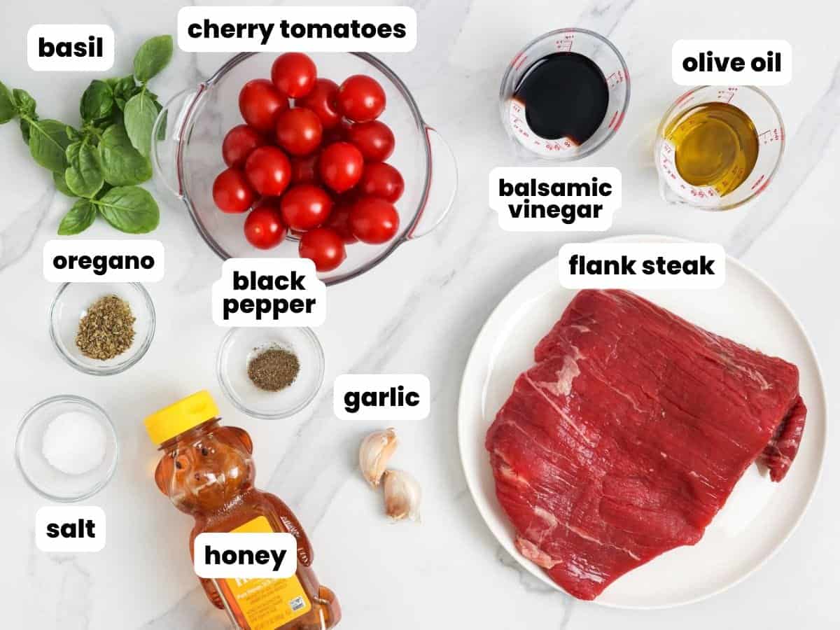 A raw flank steak on a plate next to tomatoes, basil, and seasonings needed to make Caprese steak.