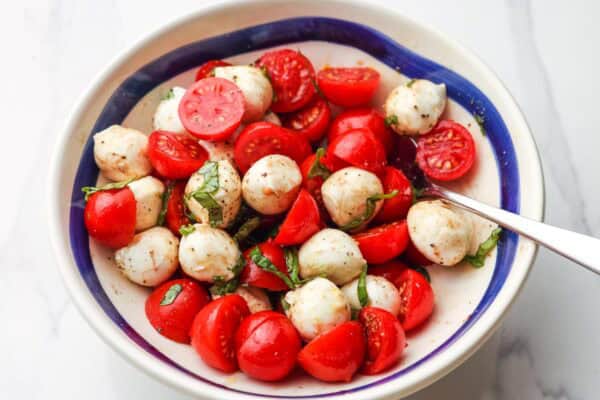 halved cherry tomatoes, small mozzarella balls, and sliced basil leaves in a bowl with balsamic dressing.