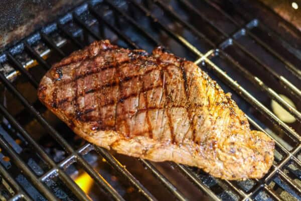 a flank steak cooking on a gas grill.