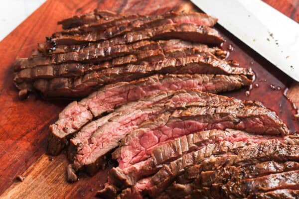 cooked flank steak, sliced thinly on a wooden cutting board.