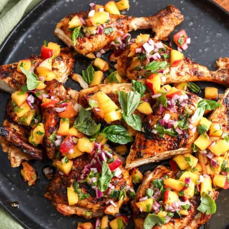 a platter of grilled cilantro lime chicken with peach salsa on top.