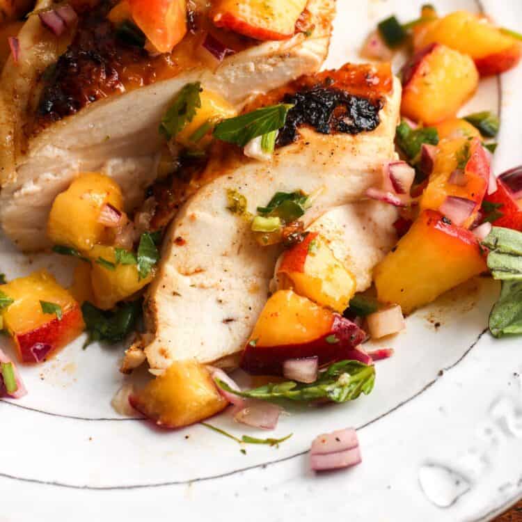 closeup of juicy sliced grilled chicken with peach salsa.