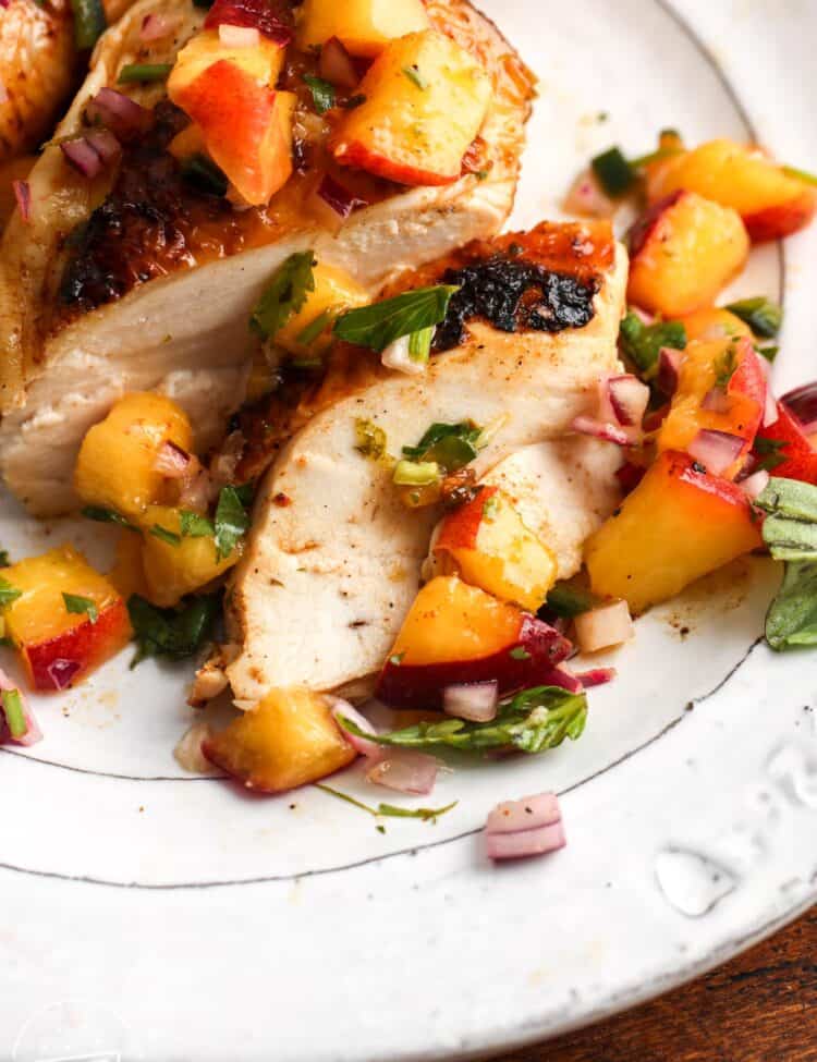 closeup of juicy sliced grilled chicken with peach salsa.