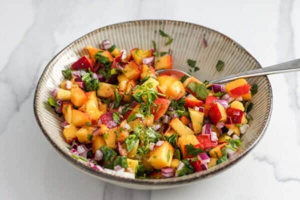 peach salsa with cilantro and red onion in a small bowl, mixed with a teaspoon.