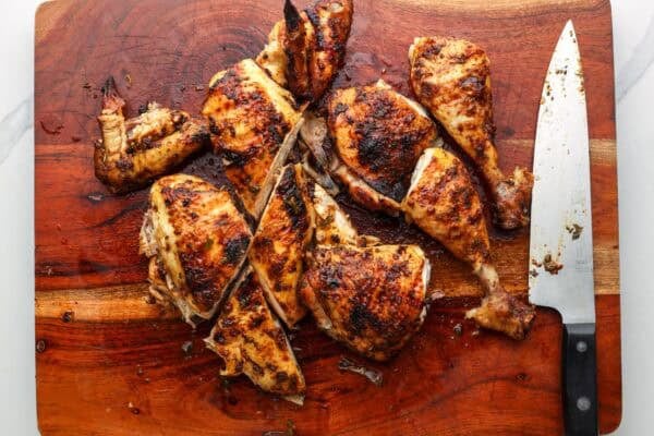 a whole spatchcock chicken cut into pieces for serving on a wooden board with a large chefs knife.