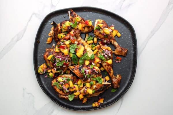 an unevenly round black plate with cilantro lime grilled chicken pieces topped with homemade peach salsa.