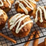 homemade cinnamon roll muffins on a wire rack. Each muffin is topped with a drizzle of white icing.