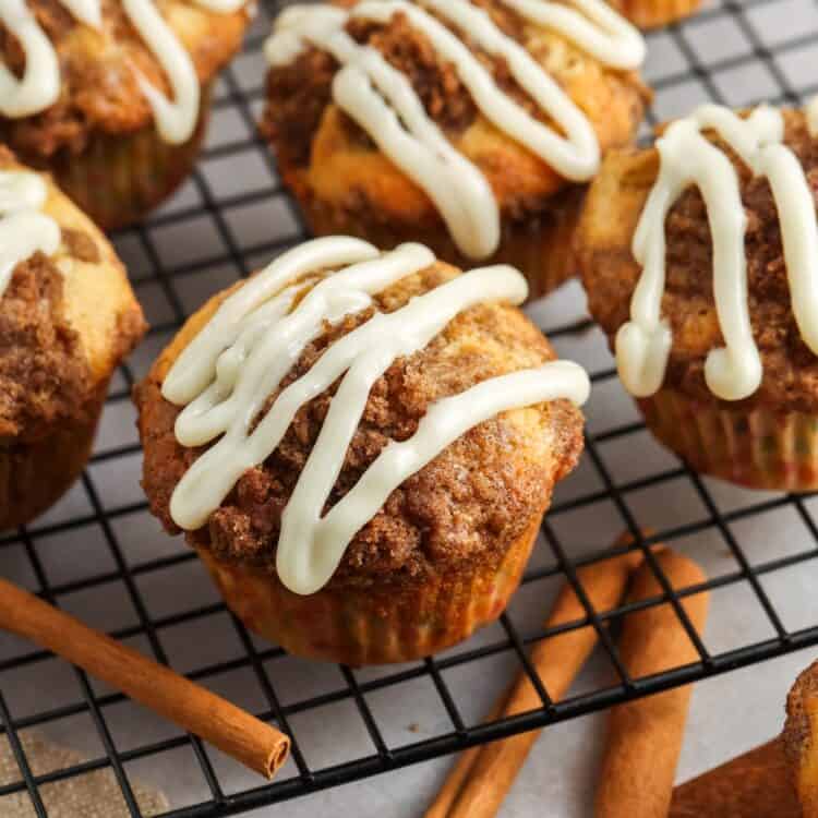 homemade cinnamon roll muffins on a wire rack. Each muffin is topped with a drizzle of white icing.