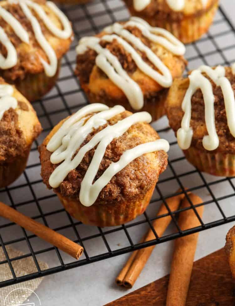 homemade cinnamon roll muffins on a wire rack. Each muffin is topped with a drizzle of white icing.