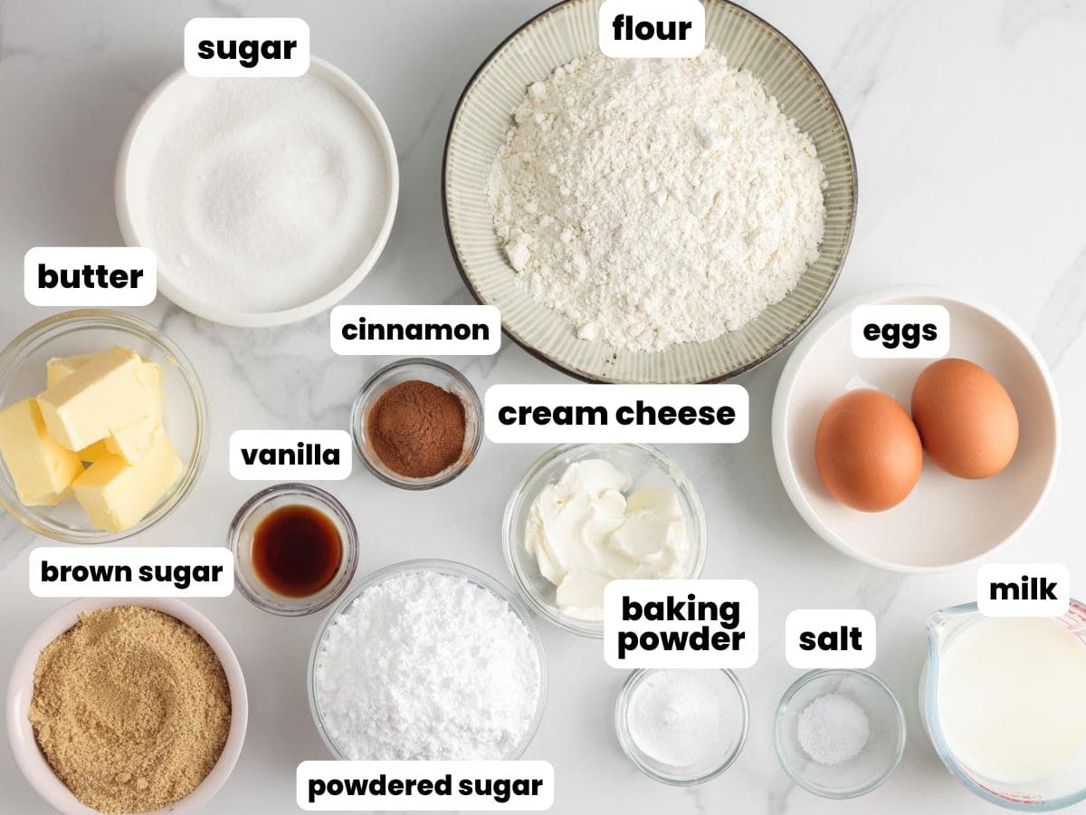 The ingredients for cinnamon roll muffins measured into separate bowls and arranged on a marble surface.