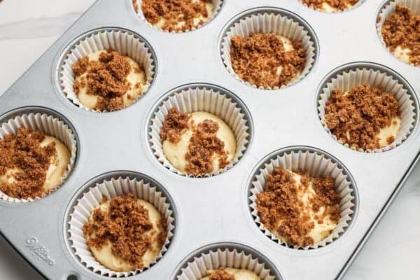 a metal muffin pan lined with papers, filled with muffin batter and topped with cinnamon sugar mixture.
