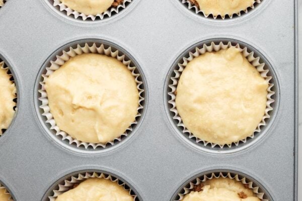 more muffin batter covering the cinnamon sugar mixture inside of muffins.