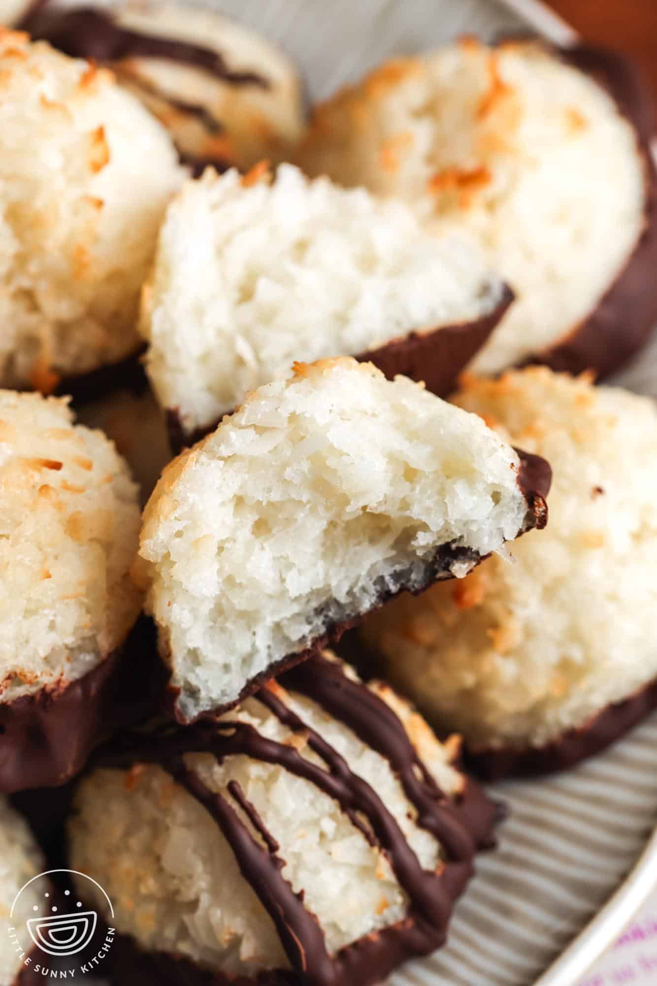 closeup of a plate of coconut macaroons dipped in chocolate. One has been pulled apart to show the texture.