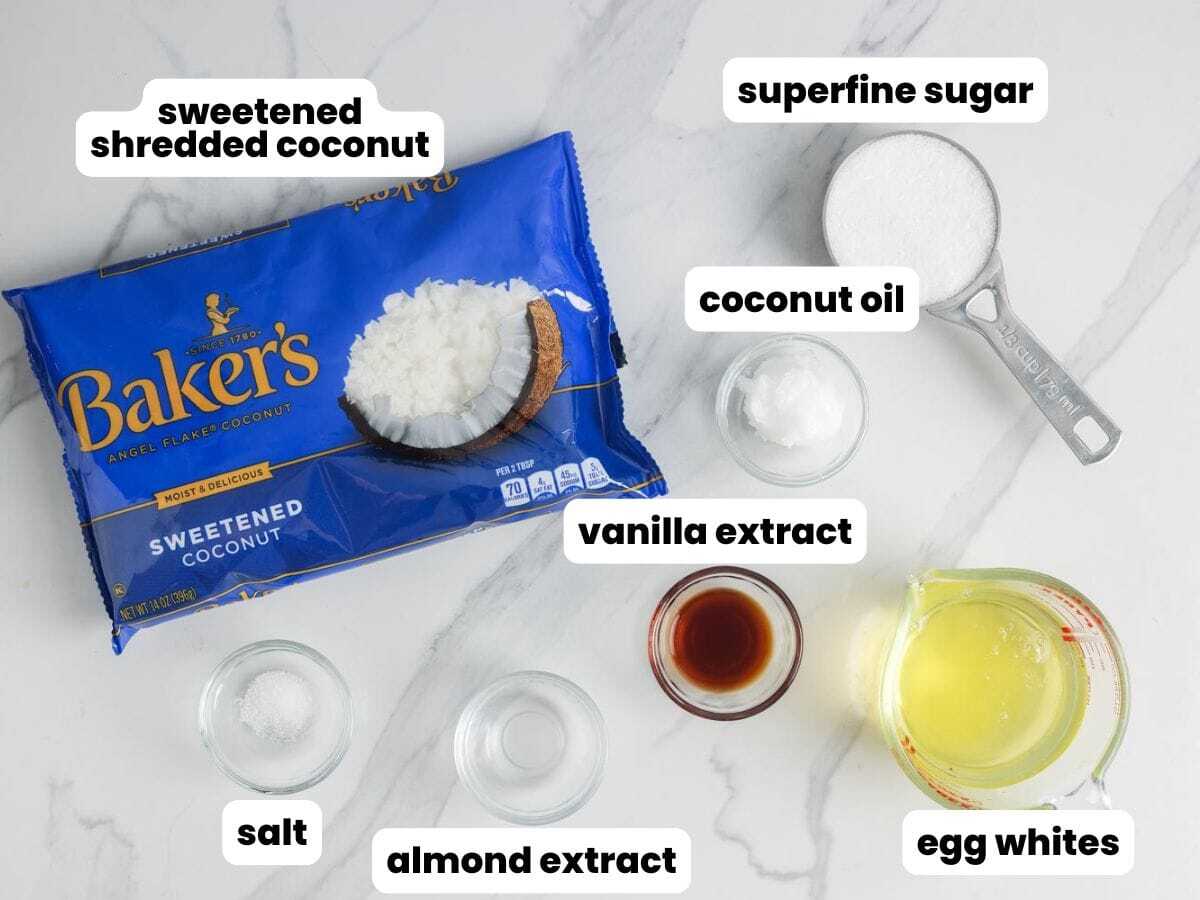 A bag of sweetened coconut, with small bowls of coconut oil, egg whites, superfine sugar, salt, and vanilla extract. These are the ingredients for making gluten free coconut macaroons.