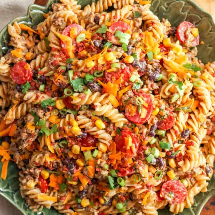 a green ceramic bowl filled with cowboy pasta salad, set on a wooden table.