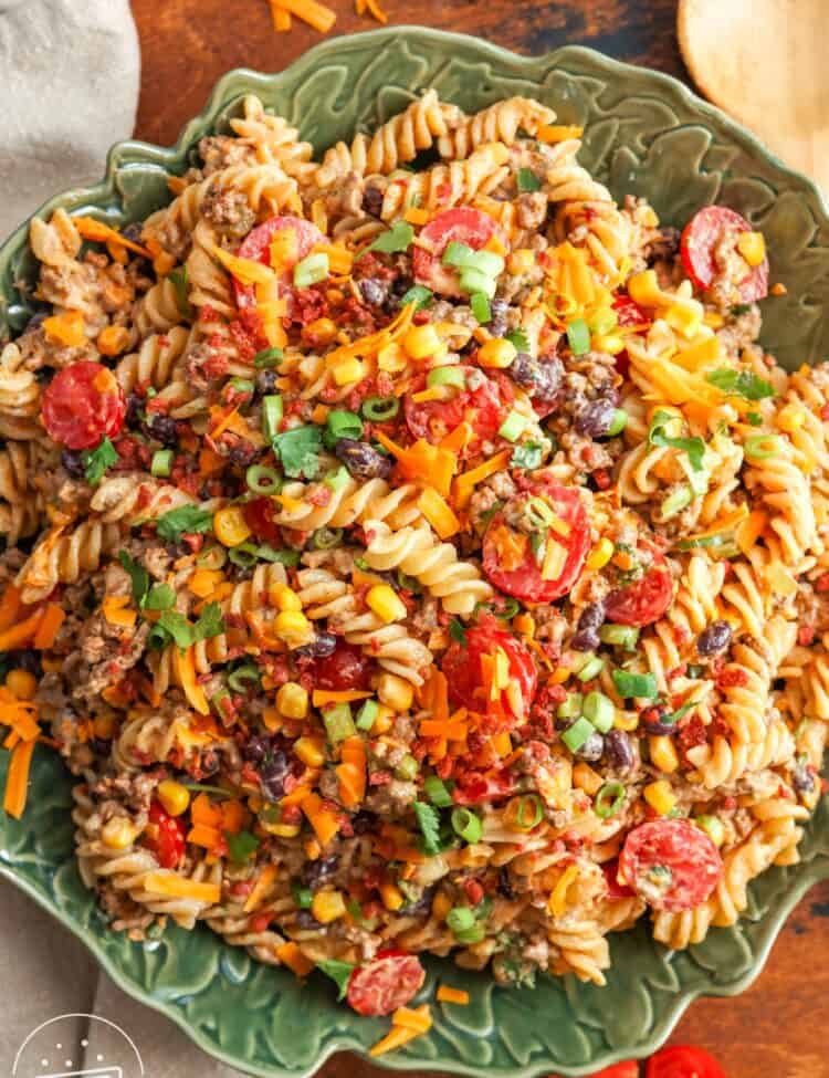 a green ceramic bowl filled with cowboy pasta salad, set on a wooden table.