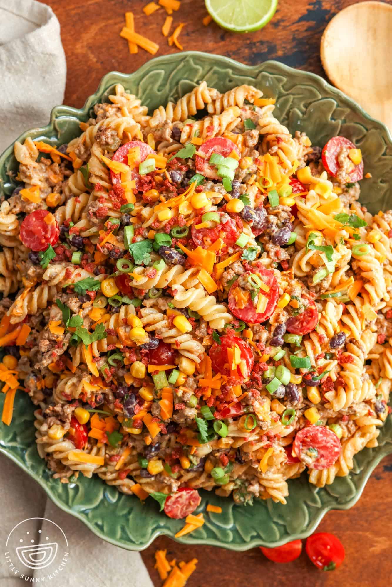 a green ceramic bowl filled with cowboy pasta salad, set on a wooden table.