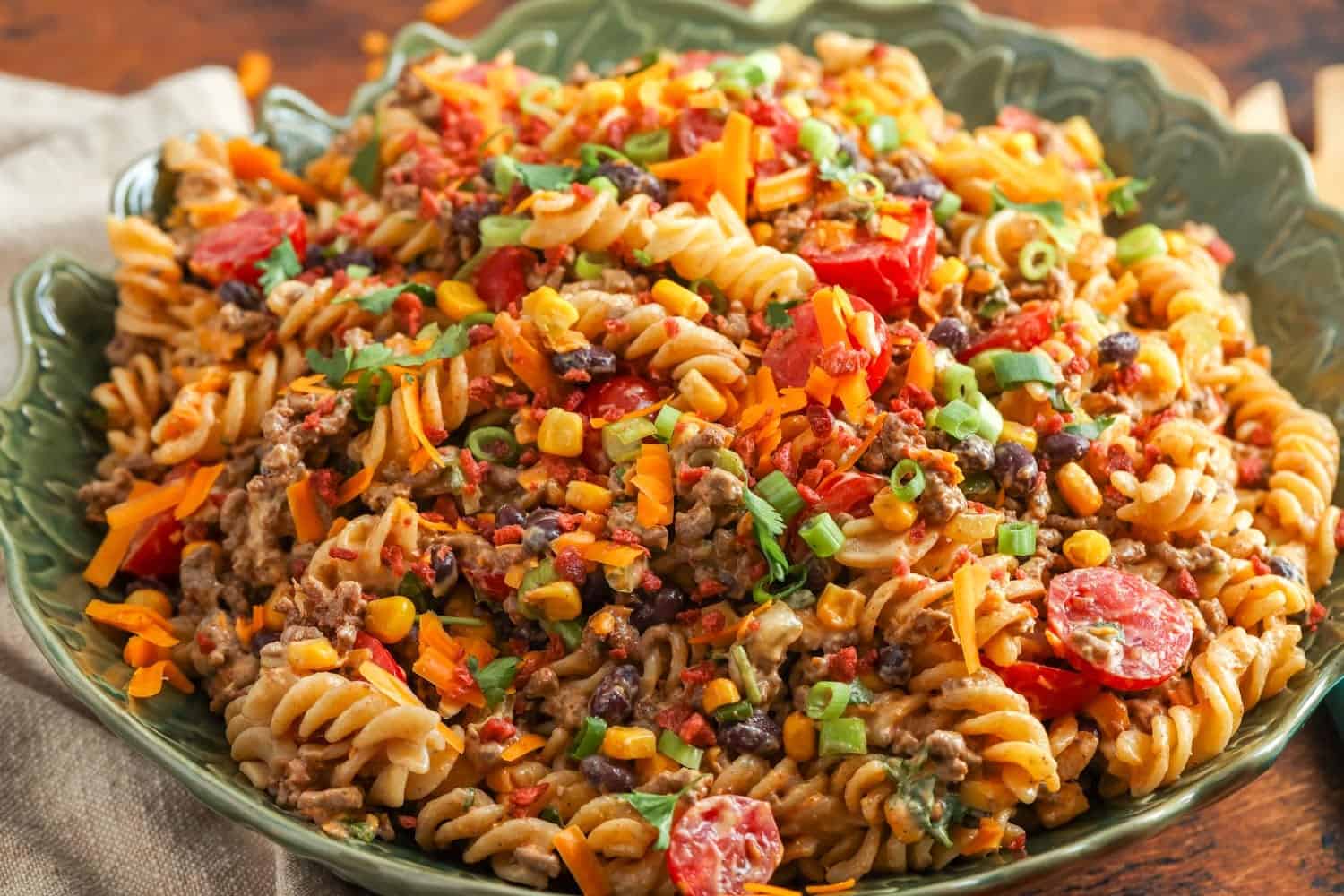 a green ceramic bowl filled with cowboy pasta salad, set on a wooden table.