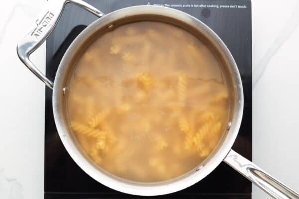 rotini noodles cooking in a pot of boiling water, viewed from above.