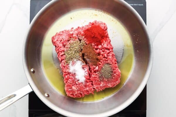 seasoned ground beef cooking in a skillet with olive oil.