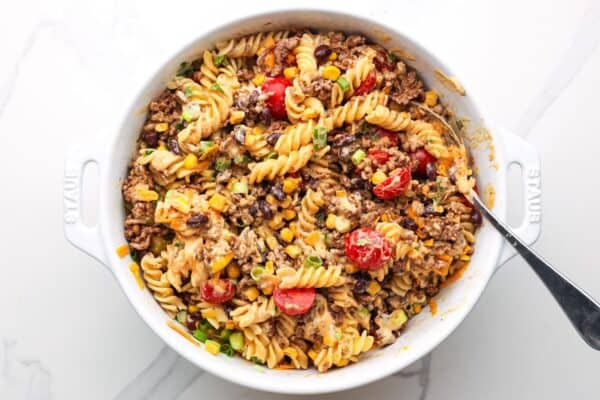 creamy cowboy pasta salad in a large white bowl, stirred with a spoon.
