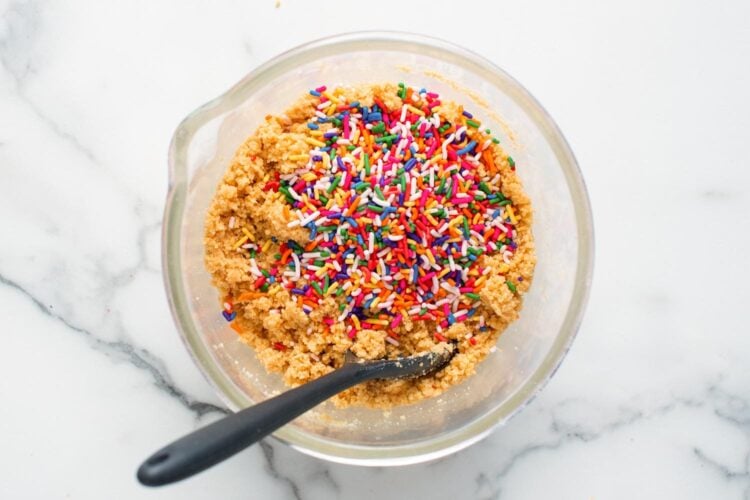 rainbow sprinkles added to a bowl of crushed cookies to make crust for funfetti cheesecake.