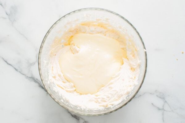 white chocolate ganache mixed into funfetti cheesecake batter in a glass bowl.