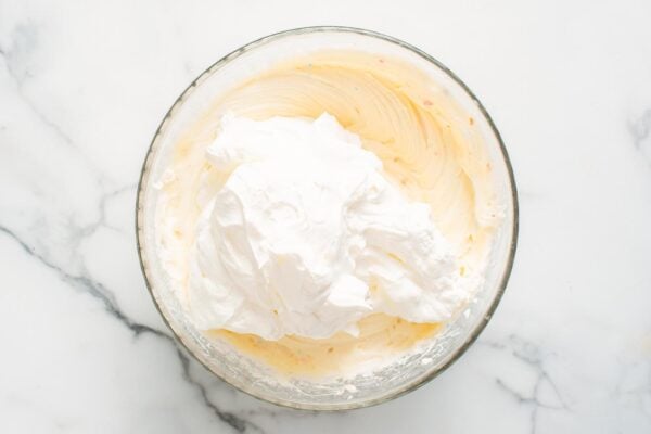 fluffy whipped cream folded into funfetti cheesecake batter in a large glass bowl.