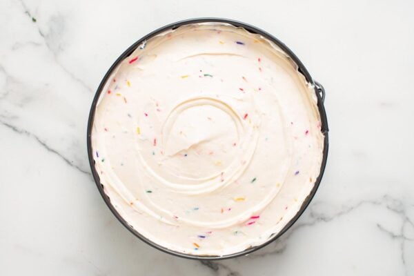funfetti cheesecake batter with rainbow sprinkles added to a springform pan and smoothed.